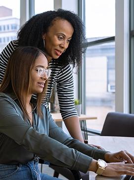 Two women collaborating on a laptop, focused on their work in a bright and modern office environment.